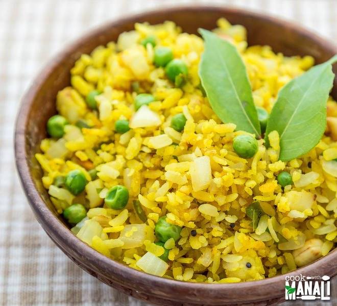 On the table has check sheet - have brown bowl filled with yellow Poha  and 2 green leaves- Healthy Indian Snacks List 